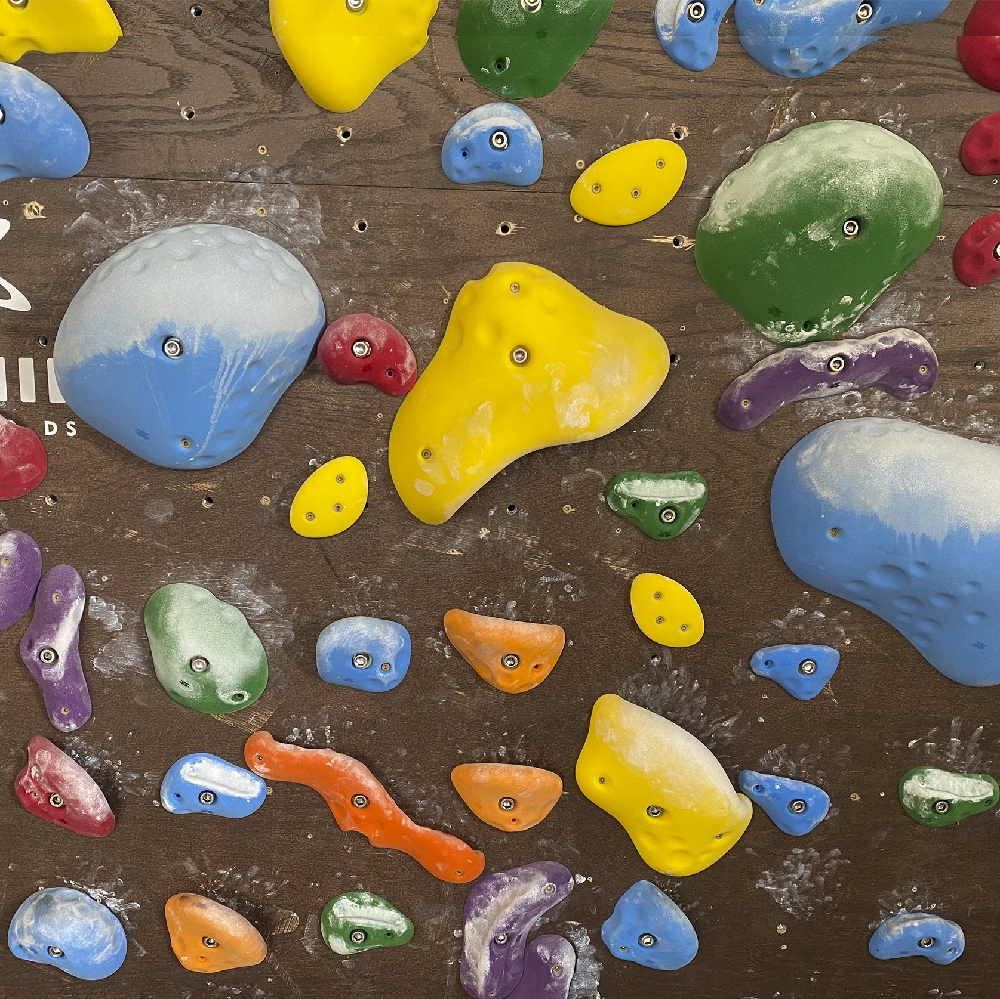 A colorful climbing wall displays chalky holds, open T-nut holes, and varied shapes across a wood panel